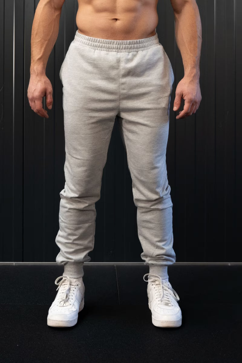 Persoon met lichtgrijze joggingbroek en witte sneakers tegen een zwarte achtergrond.