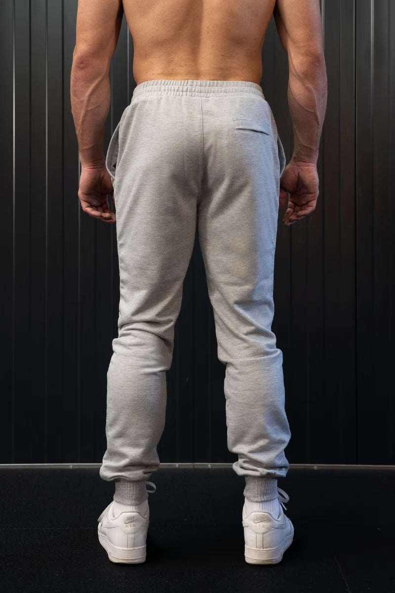 Persoon met lichtgrijze joggingbroek en witte sneakers tegen een zwarte achtergrond.