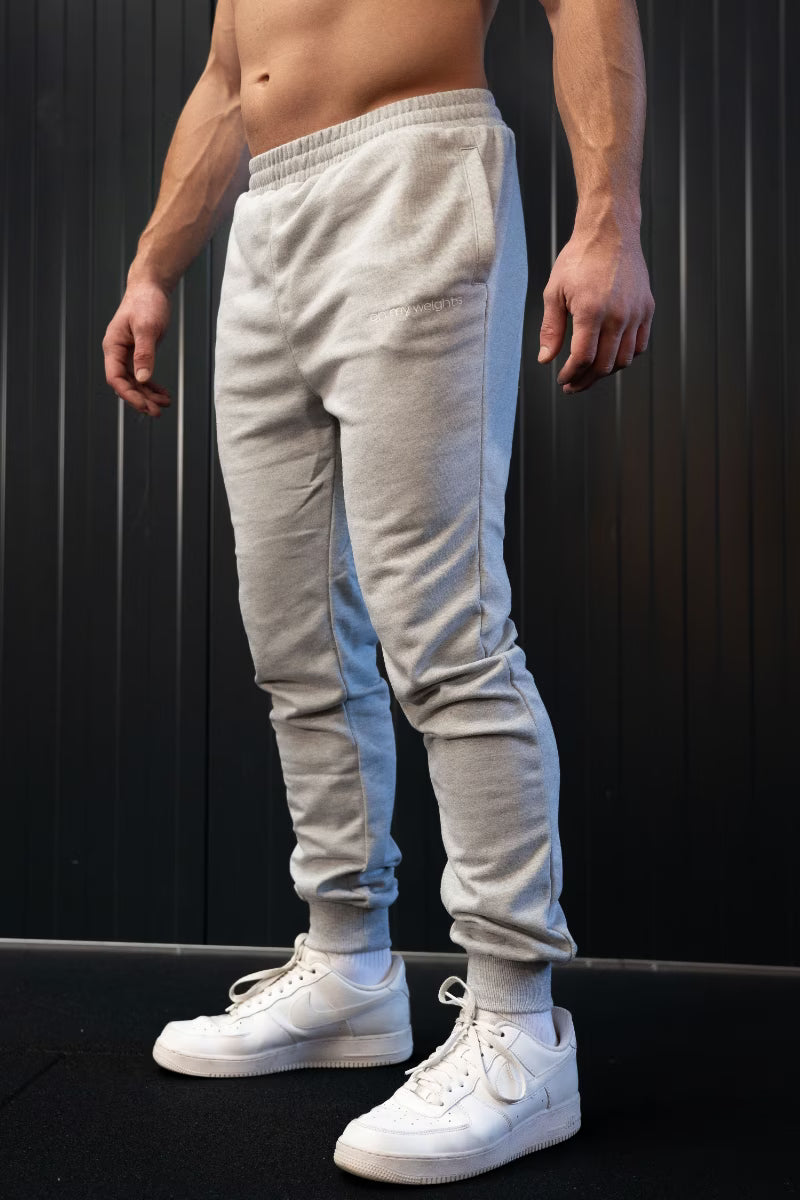 Persoon met grijze joggingbroek en witte sneakers tegen een donkere achtergrond.