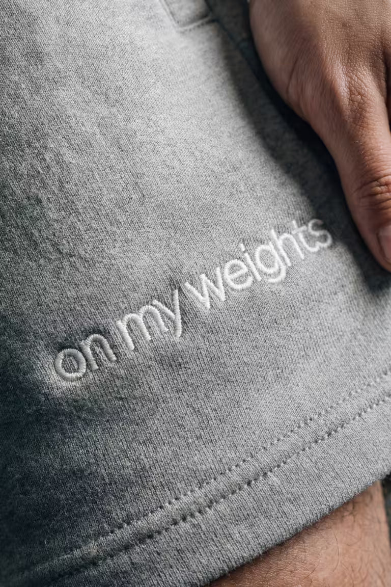 Grijze korte broek met de tekst 'on my weights' geborduurd op het been van een persoon.