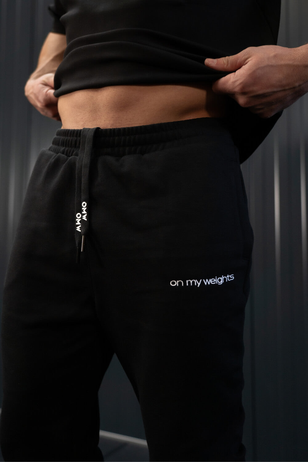 Close-up of On My Weights joggers logo and drawstrings – detail van zwarte sportbroek met OMW branding.