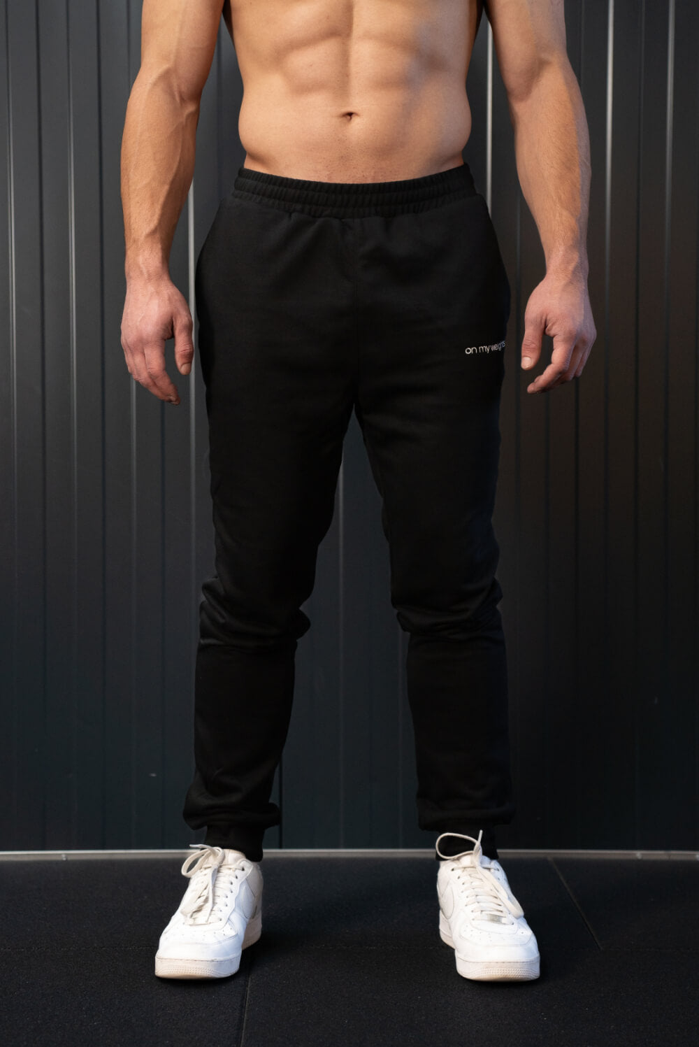 Man wearing black On My Weights joggers – comfortabele zwarte sportbroek voor heren, studiofoto met witte sneakers.