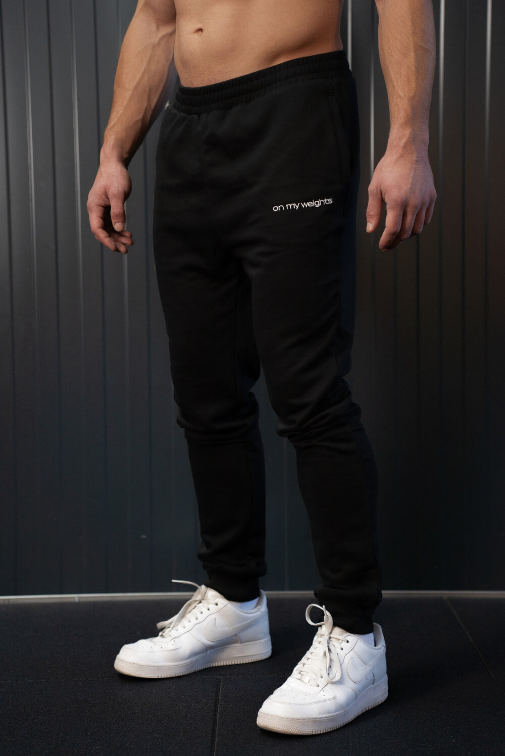 Model in zwarte On My Weights joggers, sporty fit met subtiel logo op het been – gymwear fashion for men.
