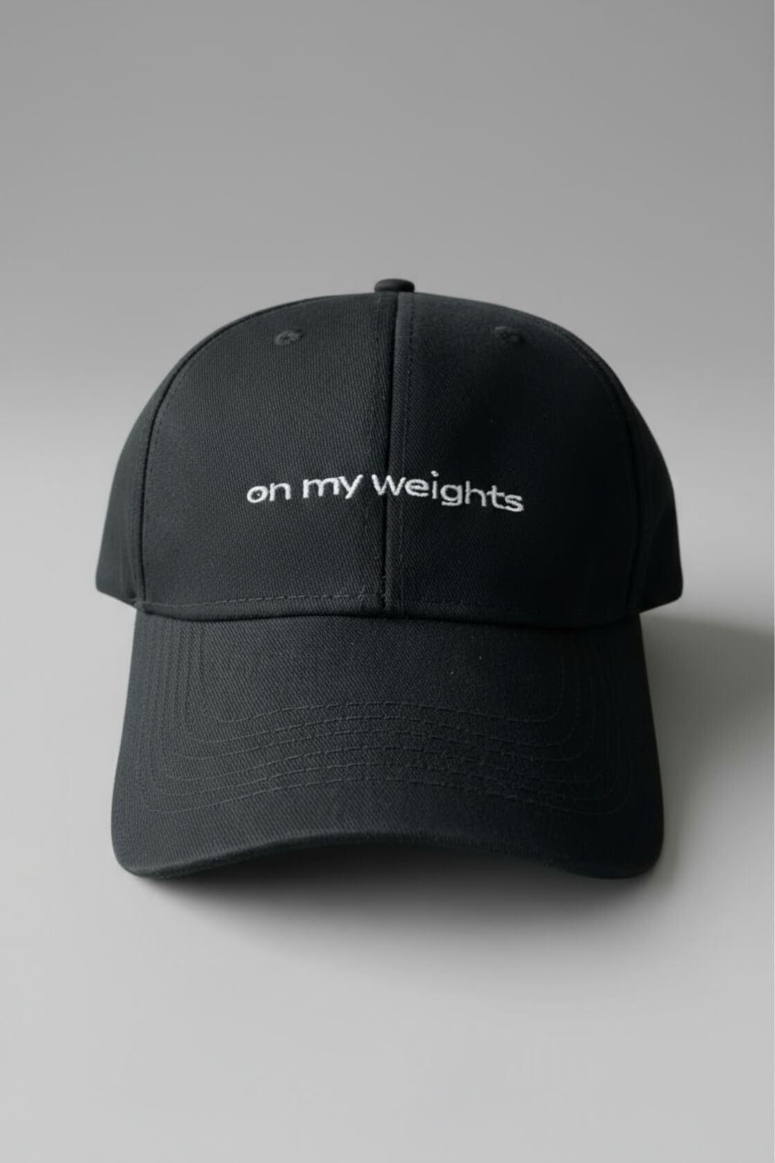 Front view of the OMW black dad hat centered on a light-gray seamless surface, white “on my weights” embroidery prominently displayed on the front panel, bill curved naturally, soft drop shadow, high-detail product shot.