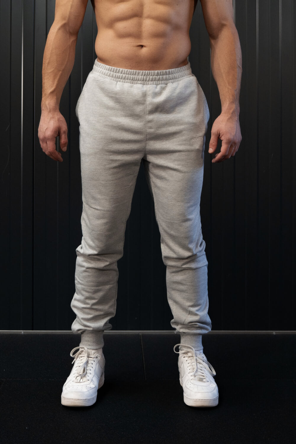 Man wearing grey On My Weights joggers – comfortabele grijze sportbroek voor heren, casual gym look met witte sneakers.