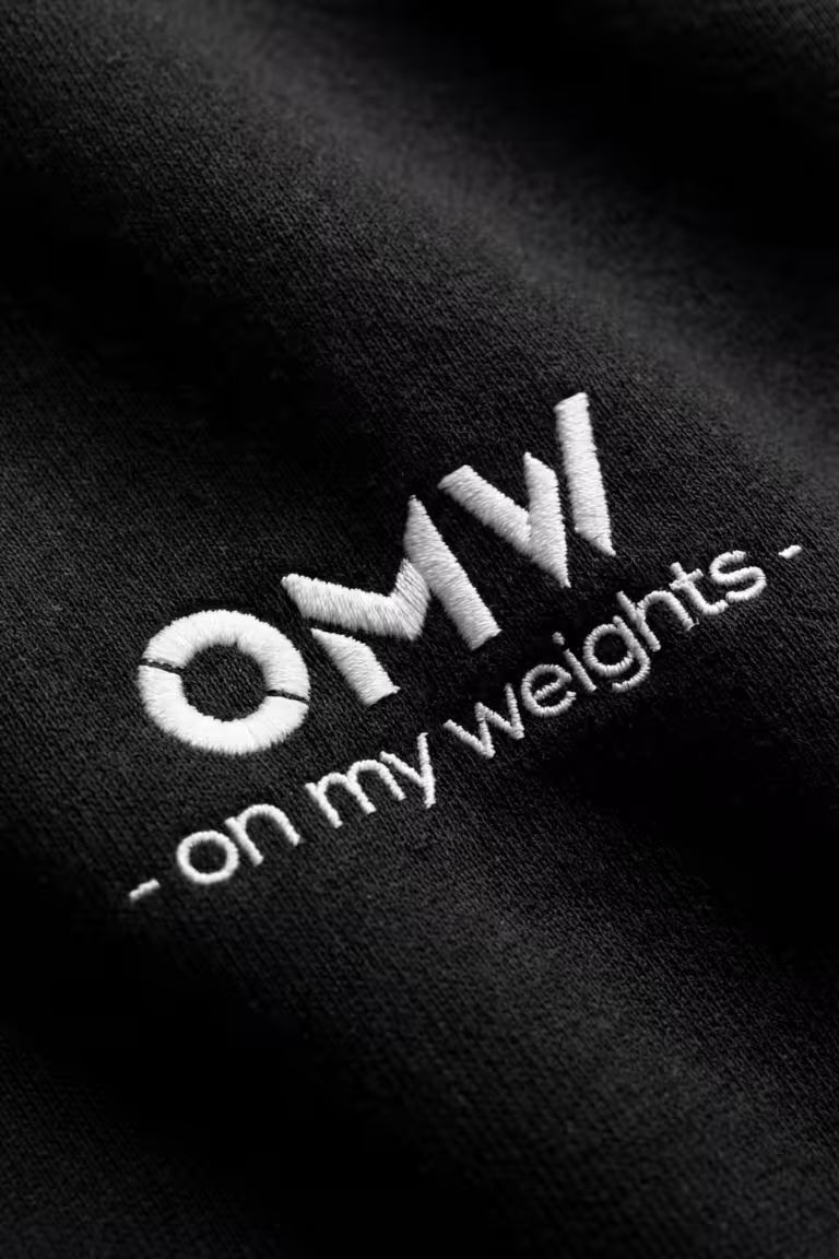 Zwarte hoodie met het 'On My Weights'-logo in wit geborduurd op een donkere achtergrond.