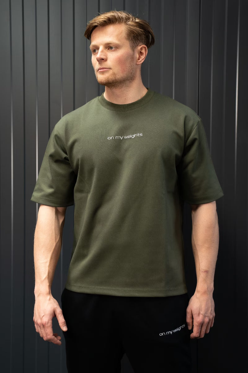 Man met een groen T-shirt met het logo 'on my weights' op een donkere achtergrond.