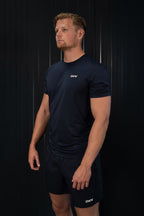 Man in een marineblauwe sportoutfit met een logo op een zwarte achtergrond.