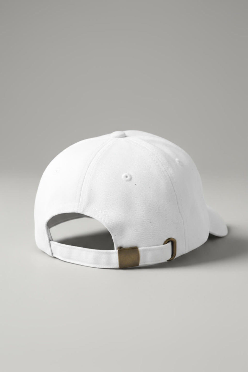 Rear three-quarter view of the OMW white dad hat resting on a light-gray studio floor, showing the adjustable strap with brass buckle and D-ring, subtle dust specks on pitch-black cotton twill fabric, ultra-sharp product photography.