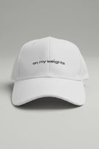 Witte pet met de tekst 'on my weights' op een grijze achtergrond.
