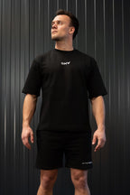 Man in een zwart t-shirt en korte broek met een OMW logo voor een donkere achtergrond.