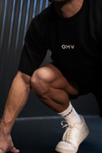 Persoon met een zwarte crewneck t-shirt met 'OMW'-logo en witte sneakers op een donkere achtergrond in een sprint pose.