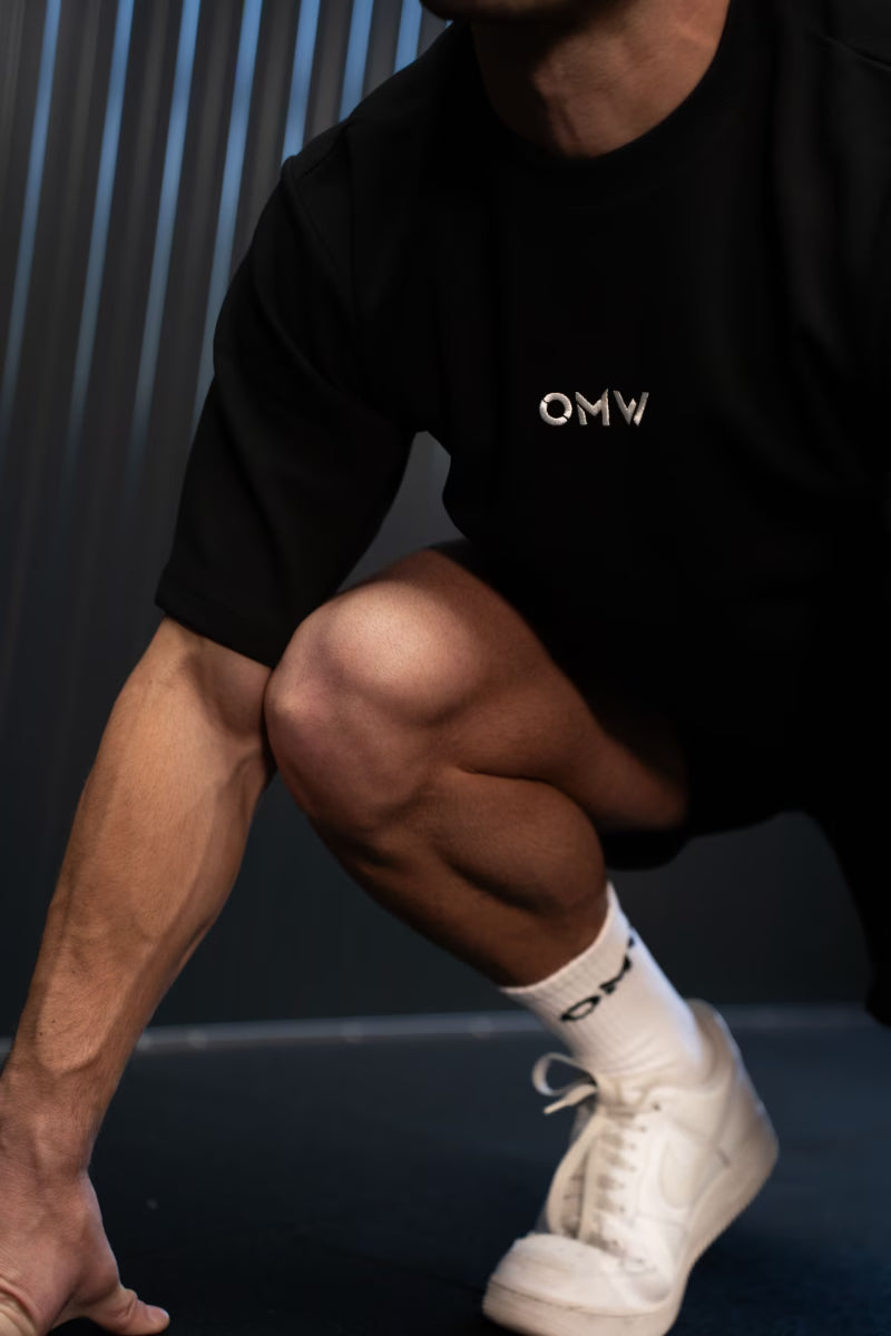 Persoon met een zwarte crewneck t-shirt met 'OMW'-logo en witte sneakers op een donkere achtergrond in een sprint pose.