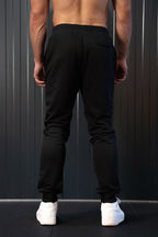 Persoon met zwarte joggingbroek en witte sneakers tegen een donkere achtergrond.